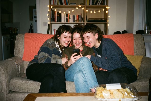 Tres amigos se ríen mirando un móvil en el sofá