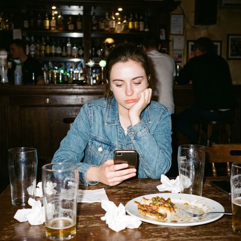Una chica espera sola en la mesa del bar mirando el móvil