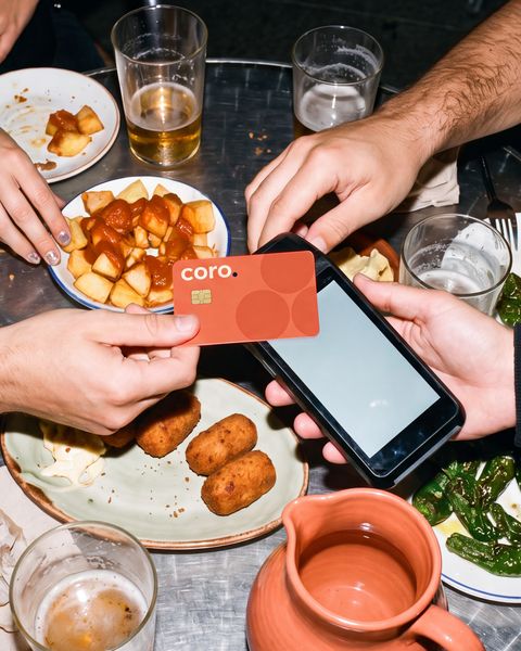 Cuatro amigos comparten tapas en una terraza de noche; uno acerca la tarjeta coral de coro al datáfono